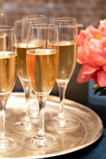 Champagne flutes on a silver tray beside pink peonies