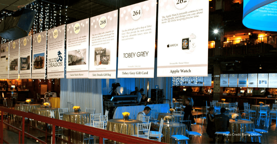 Silent auction banners hanging above cocktail tables at a fundraising gala