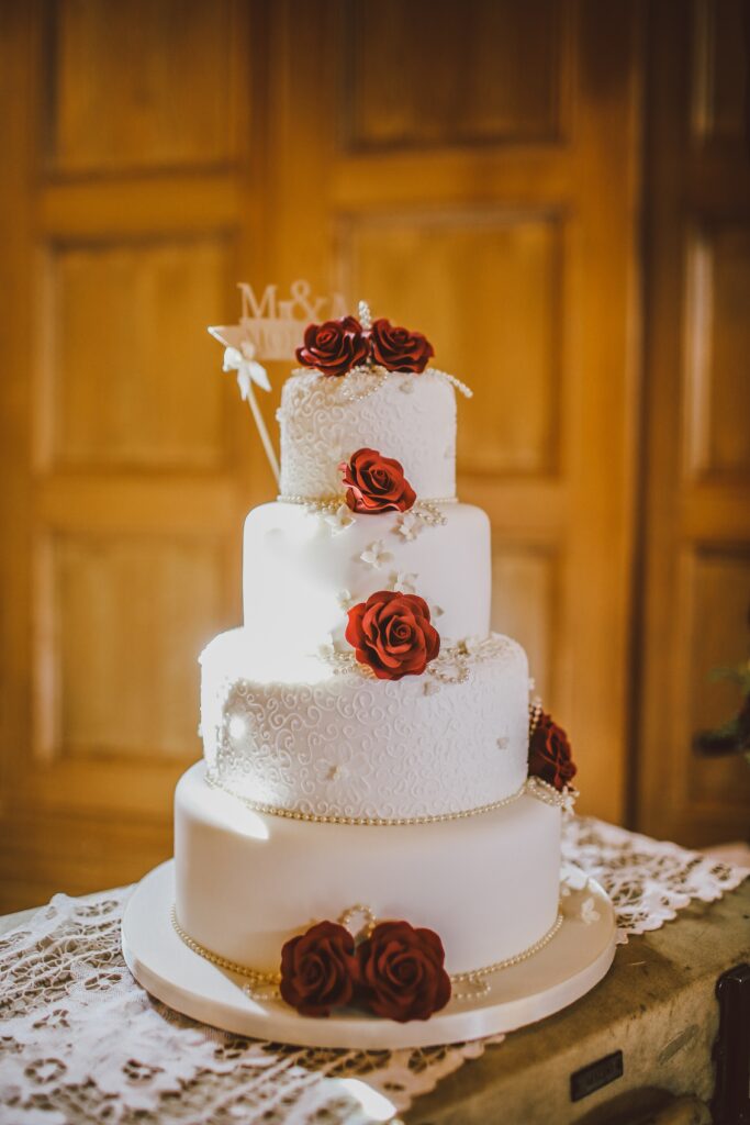 Tiered white wedding cake with red roses on a wooden backdrop
