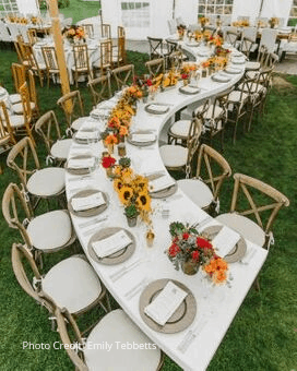 Long curved reception table with sunflowers and warm florals under a tent